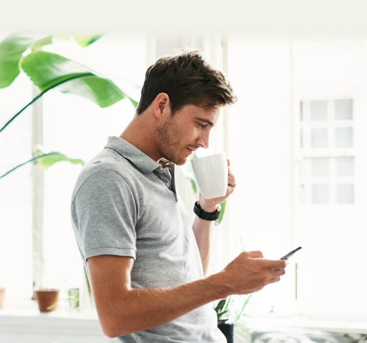Bărbat care bea cafea în timp ce ține în mână telefonul mobil