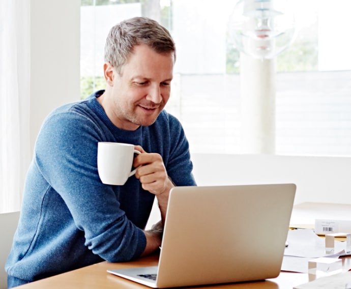 Bărbat la domiciliu folosind un laptop și bând cafea.