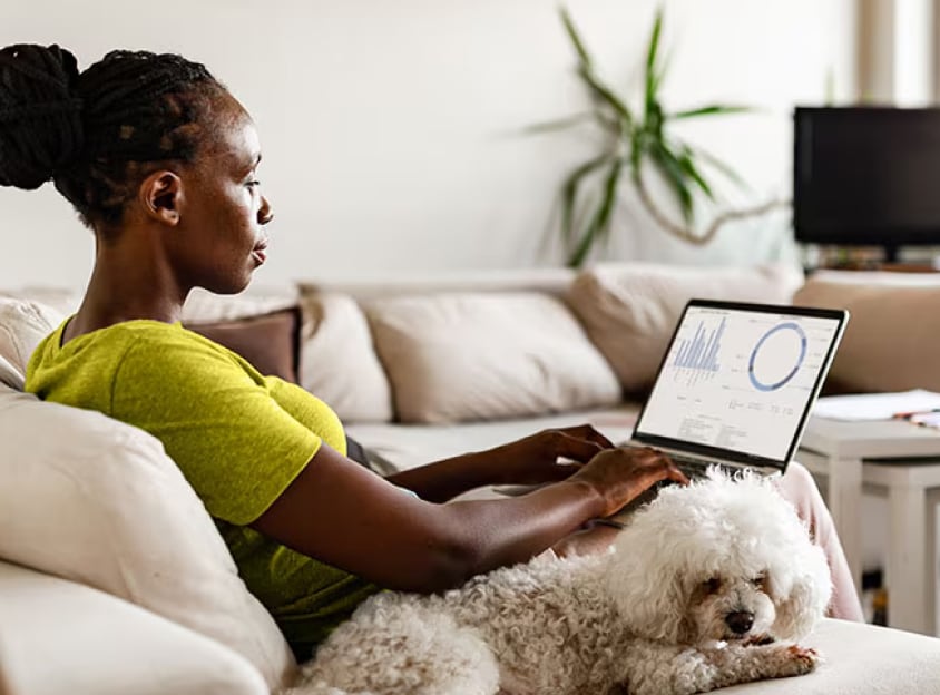Femeie stând joc cu un câine, lucrând la laptop