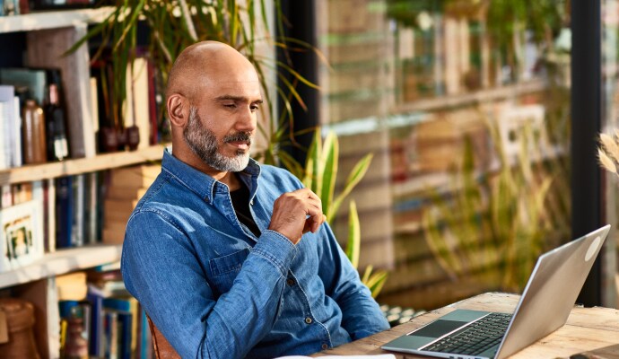 Un bărbat care stă la birou și se uită la un laptop