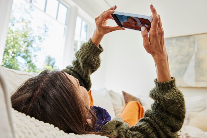 O femeie întinsă se uită la un telefon mobil